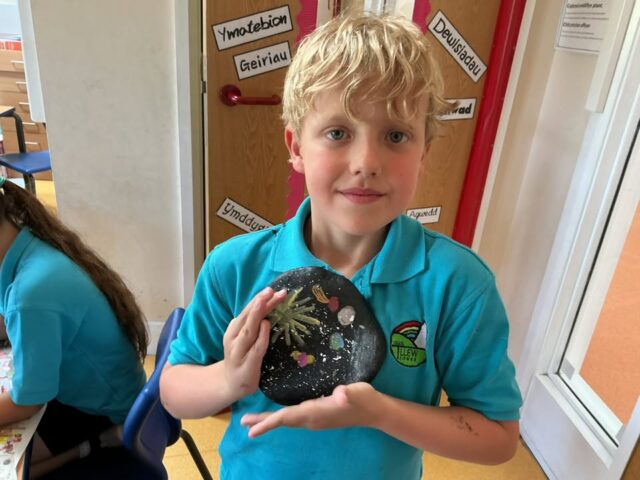 Mae disgyblion yr ysgol wedi bod yn brysur yn paentio cerrig fel rhan o weithgaredd hwyliog i ledaenu caredigrwydd, hapusrwydd a charedigrwydd yn ein cymuned. Bydd y cerrig hyn yn cael eu cuddio mewn mannau diogel a diddorol yn yr ardal leol. Os byddwch yn dod o hyd i un o’r cerrig, mae “QR Cod” yn esbonio beth i wneud ar y cefn. Gweithgaredd cymunedol i annog chi i fynd am dro a rhannu bach o hapusrwydd gydag eraill. Mwynhewch yr hwyl a sbri yn chwilio am y cerrig yn ein hardal😀